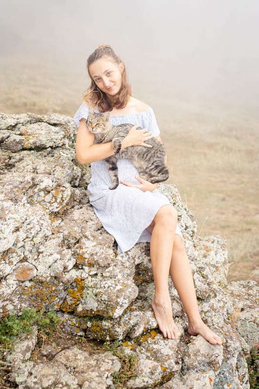 Туристка на солнечной поляне у горы Демерджи в платье позирует с котиком